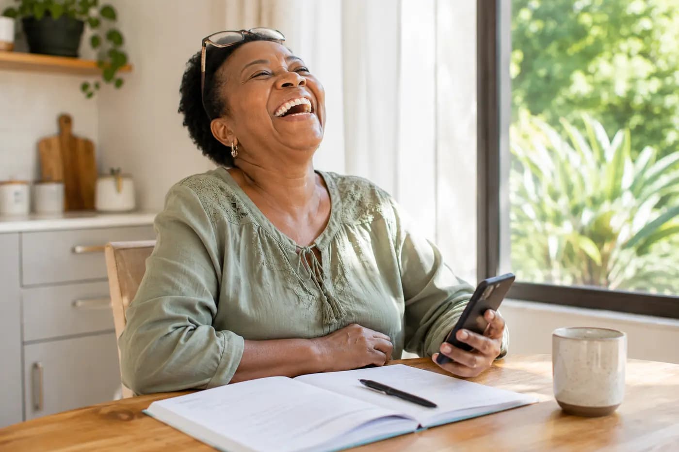 A grandmother laughing at the kitchen table, phone in hand